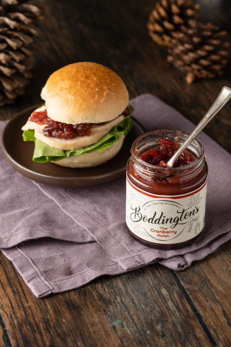 Turkey sandwich on a plate with a jar of Boddington's Cranberry Relish on a wooden surface