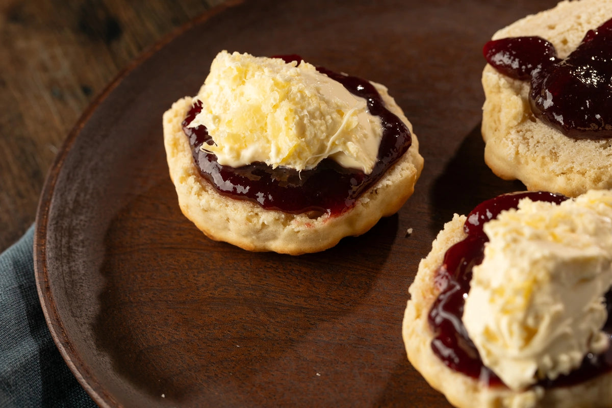 Scones with cream and damson jam on a wooden plate