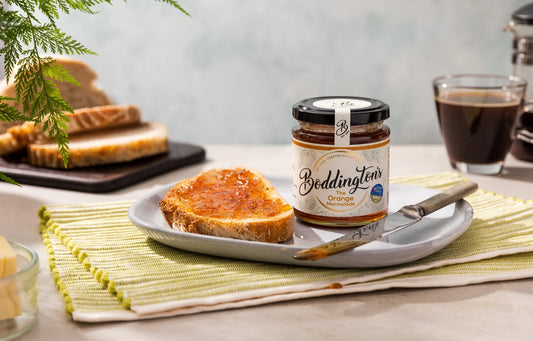Jar of Boddington's Orange Marmalade on a plate with toast and a knife, set against a neutral background.