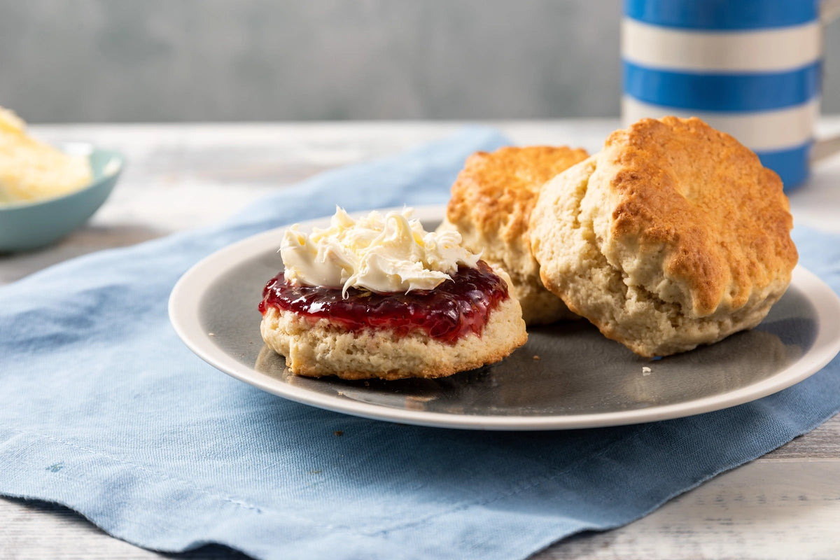 Cornish Cream tea scone on a plate with a blue napkin and striped cup in the background.