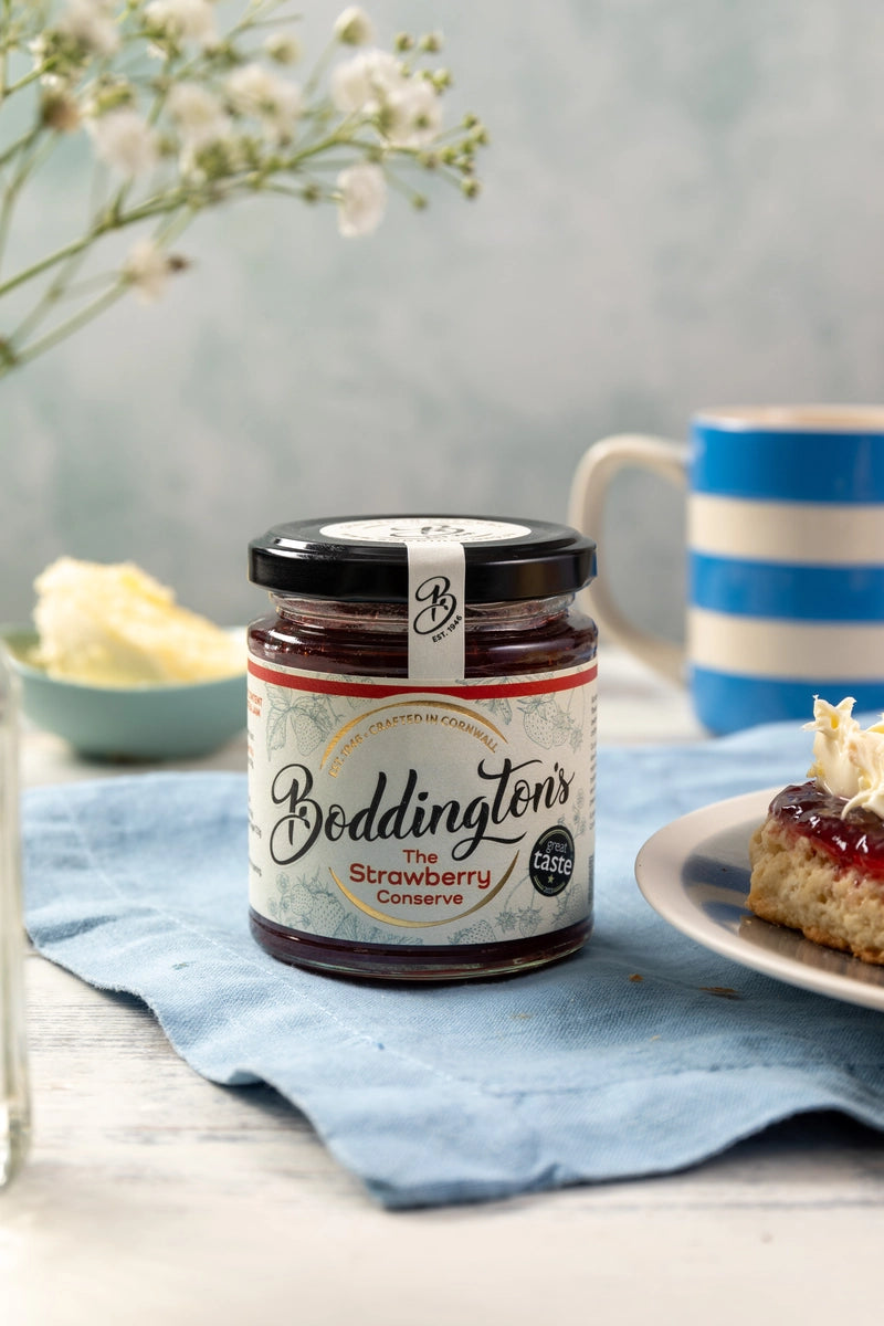 Jar of Beddington's Strawberry Jam on a table with a cup of tea and scone