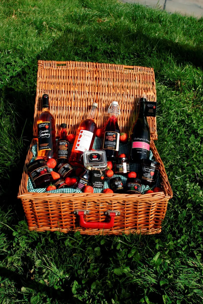 Wicker picnic basket filled with jars and bottles of strawberry products on grass