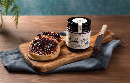 Boddingtons blackberry jam jar on a wooden board with crumpets on a wooden table.