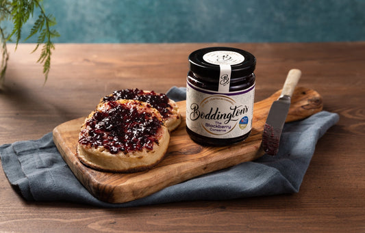 Boddingtons blackberry jam jar on a wooden board with crumpets on a wooden table.