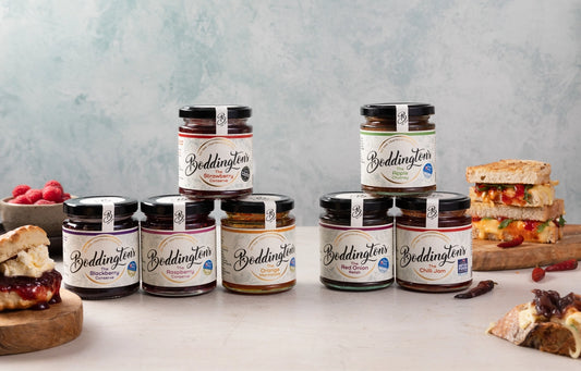 Row of Boddington's jam jars on a light background with sandwiches and fruit.