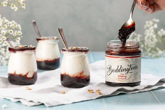 3 pots of yogurt with someone spooning jam from a jar of Cherry Conserve from Boddington's 
