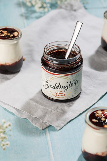 Jar of Boddington's Cherry Jam with a spoon on a light blue background