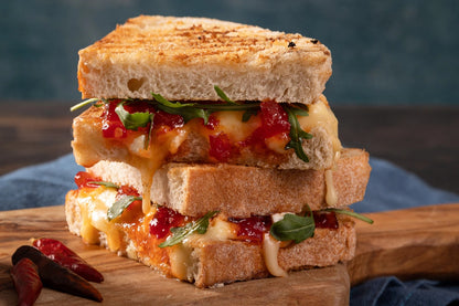 Stack of grilled cheese sandwiches with Boddington's chilli jam and rocket on a wooden cutting board.