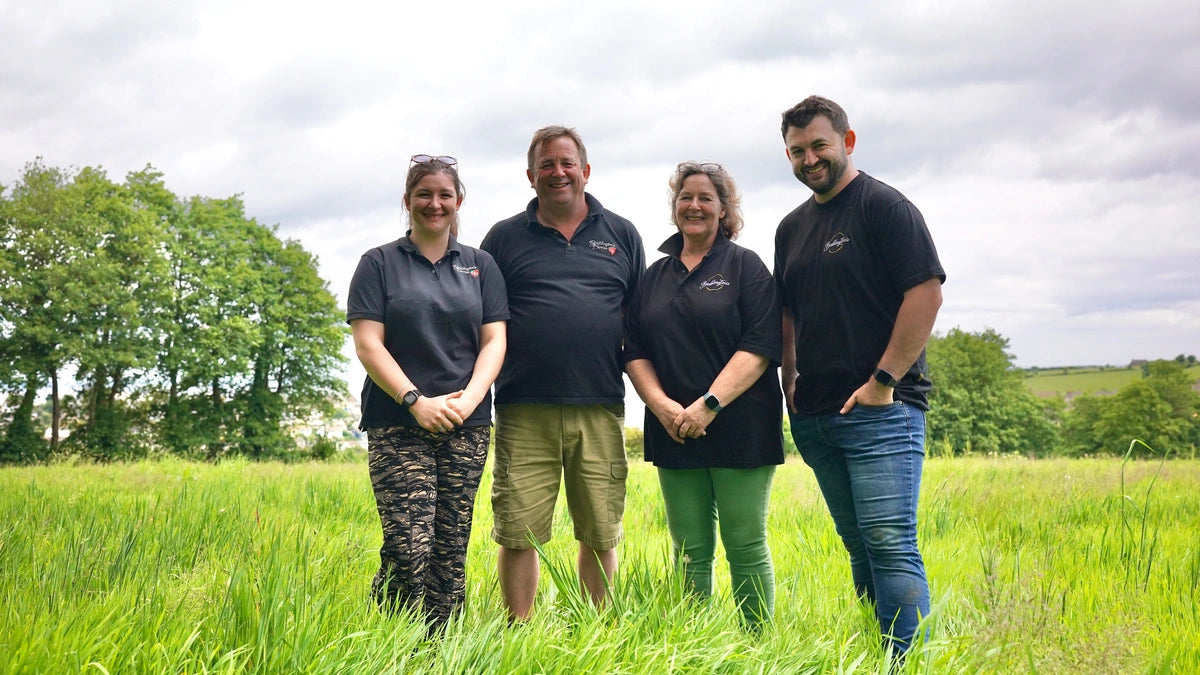 Boddington's Family Business. Third and Fouth Generation standing in a grassy field with trees and a cloudy sky in the background.