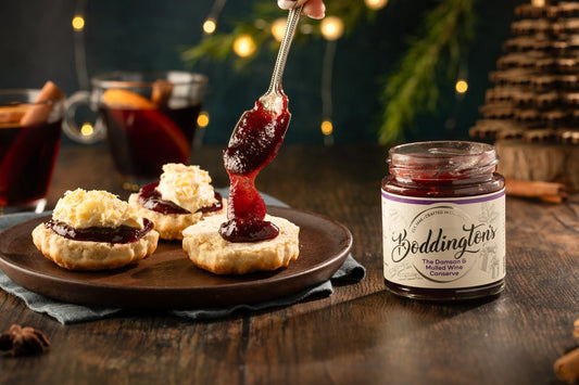Scones being spooned with Boddington's Damson and mulled wine preserve with a festive background.