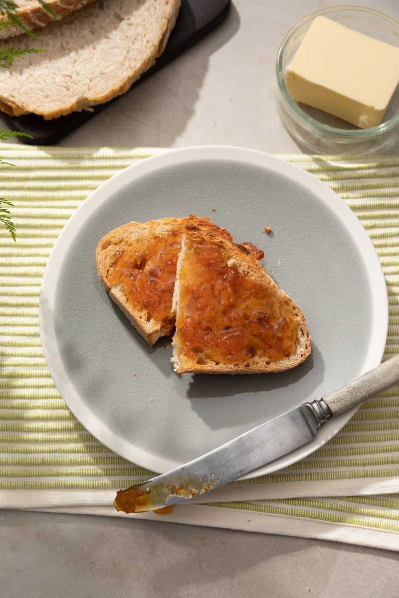 Two pieces of toast with orange marmalade and a knife on a gray plate, placed on a green and white striped mat.