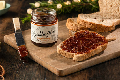 Jar of Boddington's chocolate orange marmalade on a wooden board with bread slices.