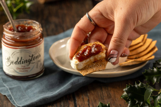 Person adding Christmas Chutney to a cracker with cheese and a jar of Boddington's in the background.